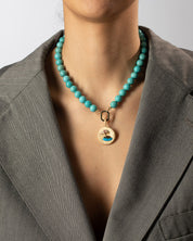 Person wearing a turquoise beaded necklace with a gold pendant against a neutral background