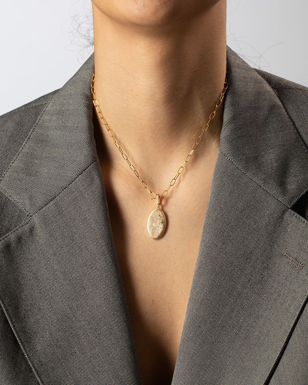 Person wearing a gold necklace with a pendant against a neutral background
