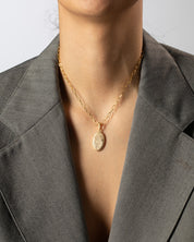 Person wearing a gold necklace with a pendant against a neutral background