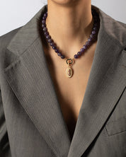 Person wearing a beaded necklace with a gold pendant against a neutral background