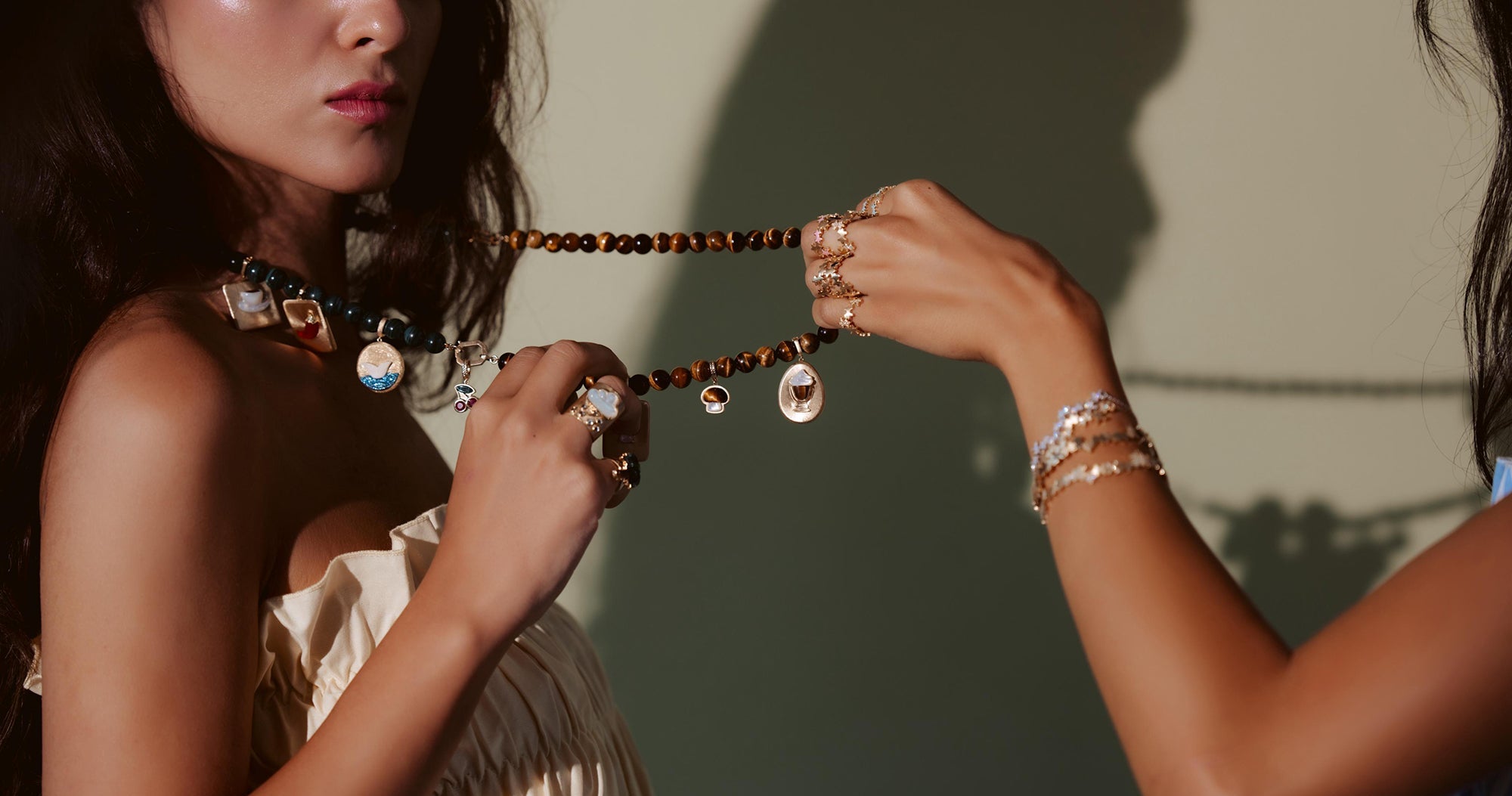 Two women holding a necklace with intricate details against a neutral background